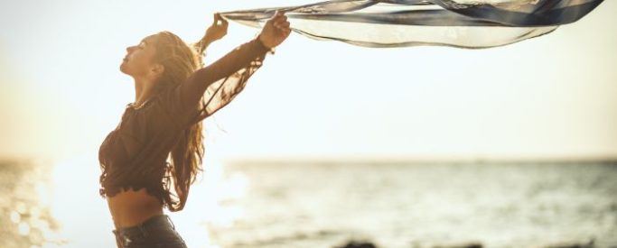 A woman on a beach with her arms raised after completing crack cocaine rehab - Step By Step Recovery